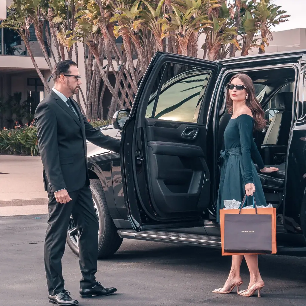 image of a chauffeur holding the door of a black car for a passenger holding bags